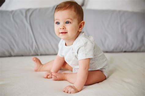 Mosolygós 8 hónapos baba, aki önállóan ül, játékokkal körülvéve