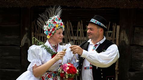Egy fiatal pár népviseletben, ölelkezve egy virágos mezőn.