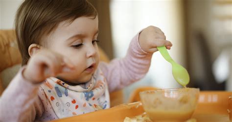 egy kisgyermek önállóan eszik a terített asztalnál