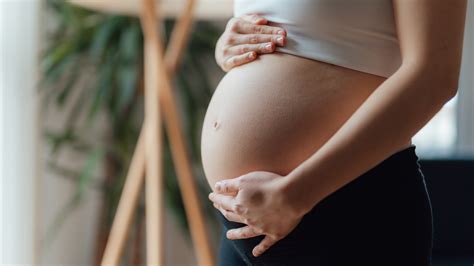 Várandós nő mosolyogva, kezét a pocakján tartva
