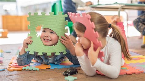 Gyermekek játszanak egy szőnyegen, színes építőkockákkal, miközben egy tanárnő angol dalokat énekel