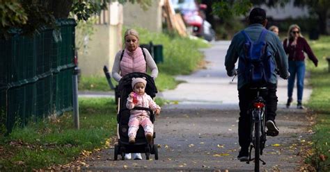 Elégedett anyuka mosolyogva tolja a babakocsiját egy parkban