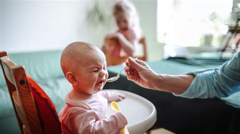 Szülő eteti a babát egy kanállal, miközben mosolyog